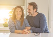 Middle-aged couple smiling in kitchen with sunset behind them